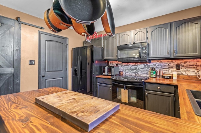 kitchen featuring gray cabinetry, wood counters, black appliances, decorative backsplash, and a barn door