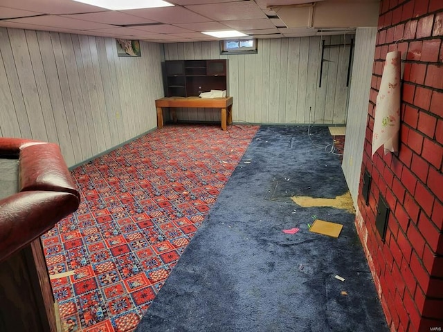 basement featuring a drop ceiling and wood walls