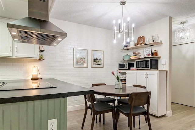 kitchen featuring pendant lighting, island exhaust hood, light hardwood / wood-style flooring, a notable chandelier, and white cabinetry