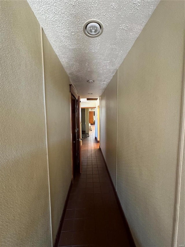 hall with a textured ceiling and dark tile patterned flooring