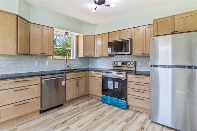 kitchen with stainless steel appliances, sink, decorative backsplash, and light hardwood / wood-style flooring