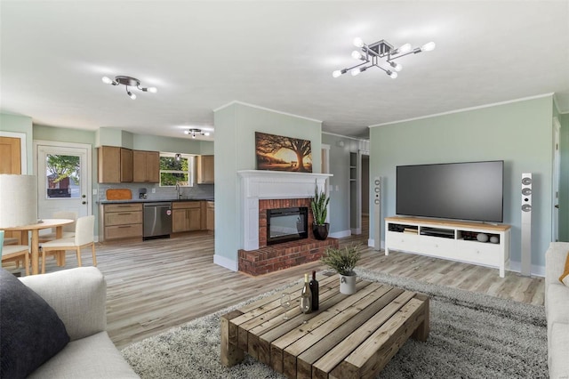 living room with a fireplace, ornamental molding, an inviting chandelier, and light hardwood / wood-style flooring