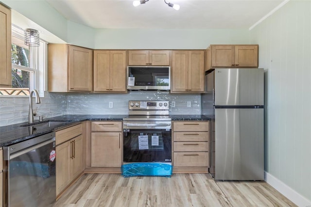 kitchen featuring stainless steel appliances, light wood-type flooring, a sink, and dark stone countertops