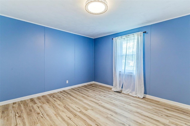 empty room featuring light wood-type flooring, baseboards, and ornamental molding