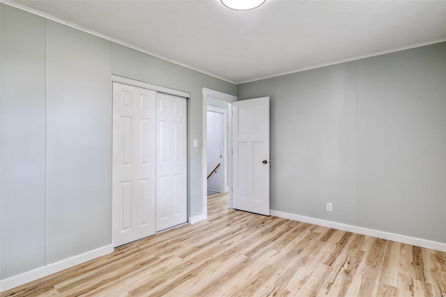 unfurnished bedroom with light wood-type flooring, a closet, baseboards, and crown molding