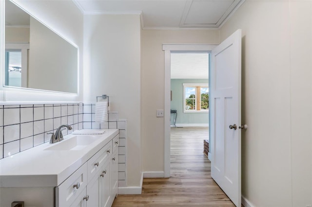 bathroom with wood finished floors, vanity, baseboards, ornamental molding, and backsplash