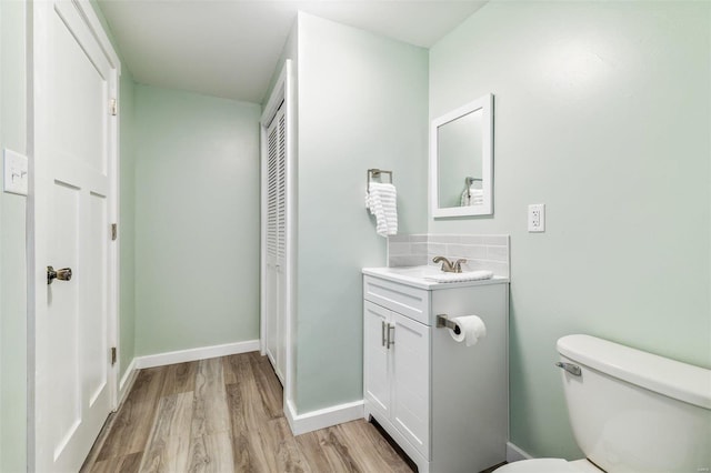 bathroom with a closet, toilet, vanity, wood finished floors, and baseboards