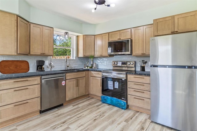 kitchen featuring light wood-style flooring, stainless steel appliances, a sink, dark stone counters, and tasteful backsplash