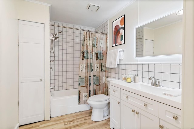 bathroom with toilet, wood finished floors, shower / bath combination with curtain, vanity, and tile walls