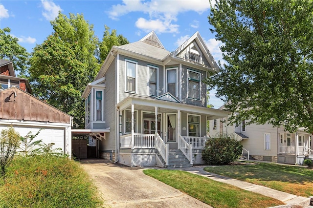 victorian-style house with a porch, a front lawn, an outdoor structure, and a garage