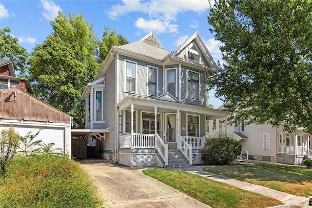 victorian house with covered porch, a garage, a front lawn, and an outdoor structure