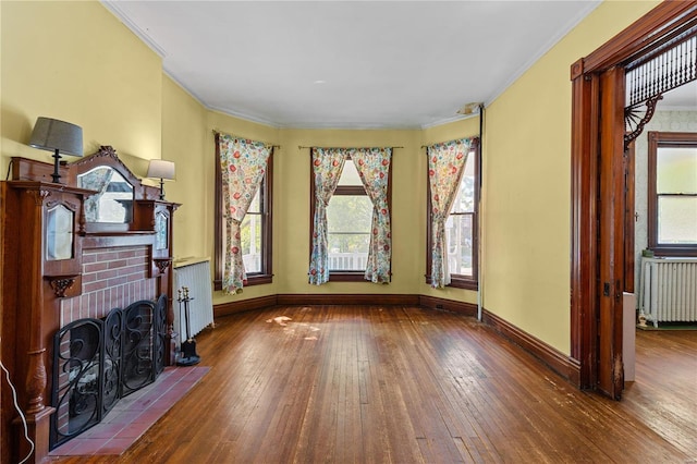 living room featuring crown molding, radiator heating unit, wood-type flooring, and a brick fireplace