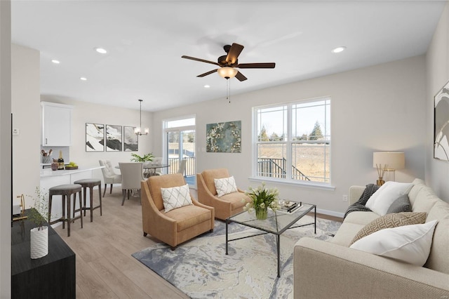 living room featuring ceiling fan with notable chandelier and light hardwood / wood-style flooring