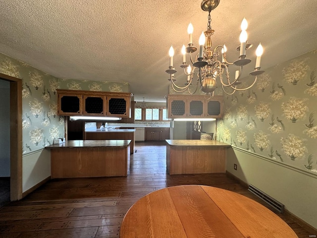 kitchen featuring a textured ceiling, kitchen peninsula, dark hardwood / wood-style flooring, and a notable chandelier