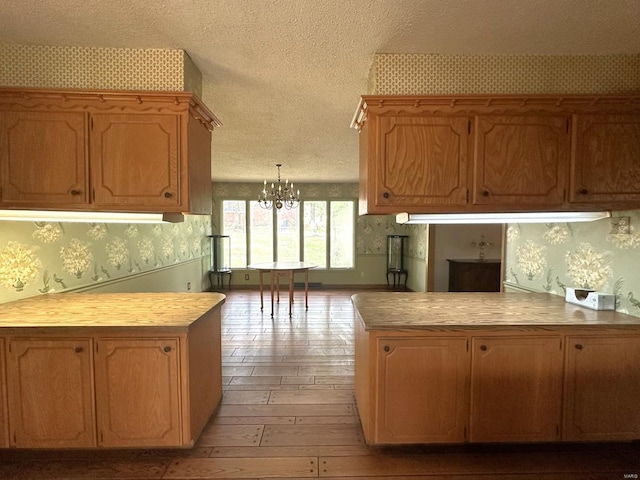 kitchen with decorative light fixtures, a notable chandelier, light hardwood / wood-style flooring, and kitchen peninsula