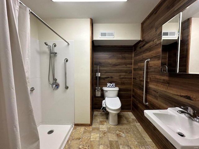 bathroom featuring a shower with curtain, sink, wooden walls, and toilet