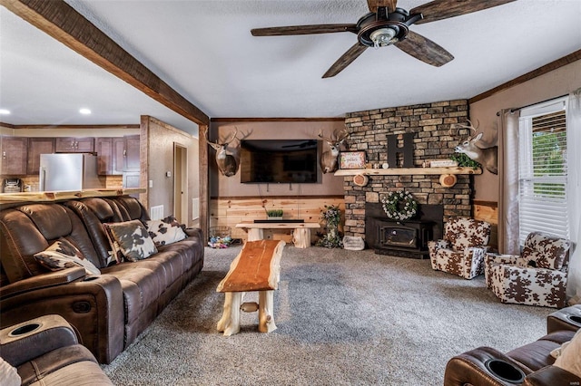 living room featuring a stone fireplace, wood walls, crown molding, ceiling fan, and carpet