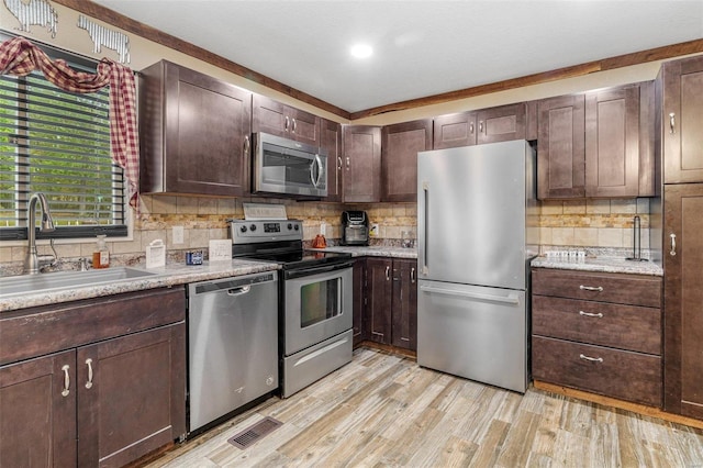 kitchen featuring dark brown cabinets, light wood-type flooring, sink, stainless steel appliances, and crown molding