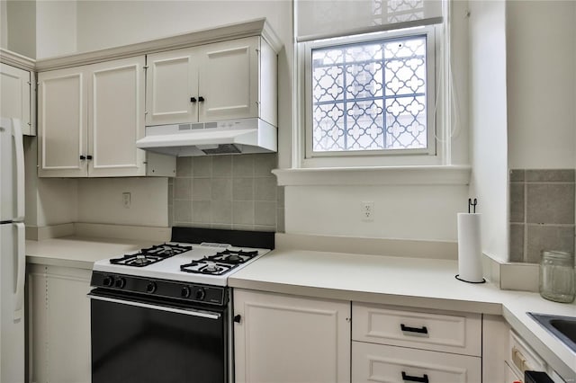 kitchen with stove, backsplash, white fridge, and white cabinetry