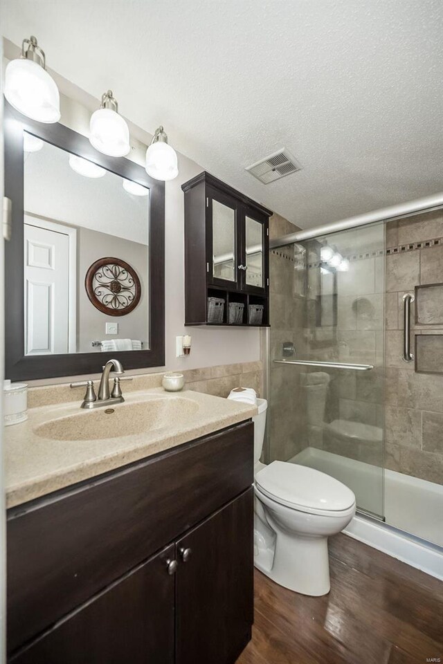 bathroom featuring vanity, hardwood / wood-style flooring, toilet, a textured ceiling, and an enclosed shower