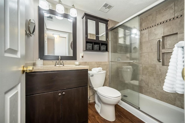 bathroom with vanity, a shower with door, hardwood / wood-style flooring, toilet, and a textured ceiling