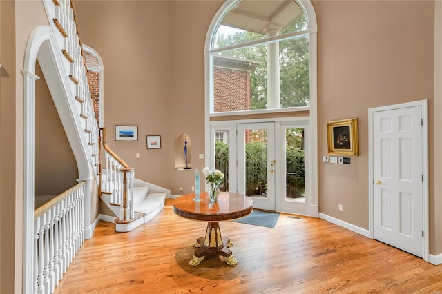 foyer entrance featuring a towering ceiling, french doors, and light hardwood / wood-style floors