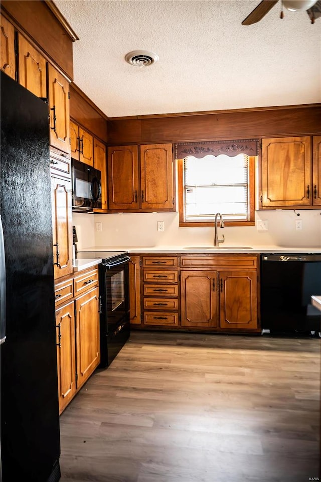 kitchen featuring ceiling fan, sink, a textured ceiling, black appliances, and light wood-type flooring