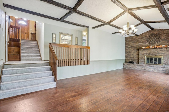 unfurnished living room featuring a brick fireplace, brick wall, a textured ceiling, dark wood-type flooring, and a notable chandelier