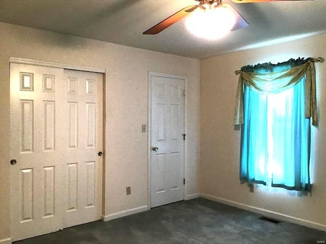 unfurnished bedroom featuring ceiling fan, dark carpet, and multiple windows