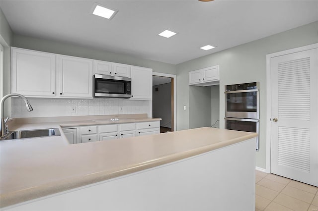 kitchen with sink, light tile patterned floors, backsplash, white cabinets, and appliances with stainless steel finishes