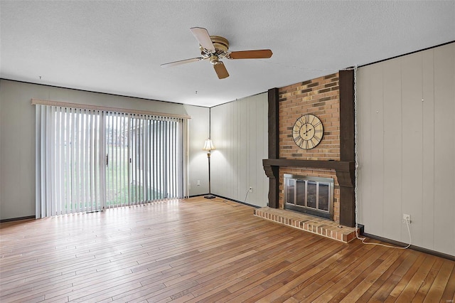 unfurnished living room featuring a brick fireplace, ceiling fan, a textured ceiling, and light wood-type flooring