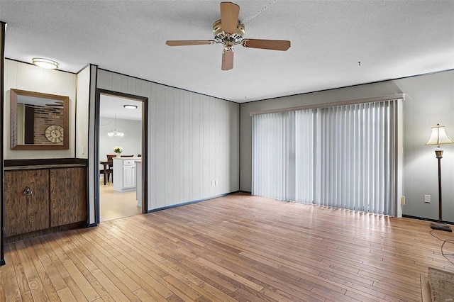 unfurnished living room with light hardwood / wood-style flooring, ceiling fan with notable chandelier, and a textured ceiling