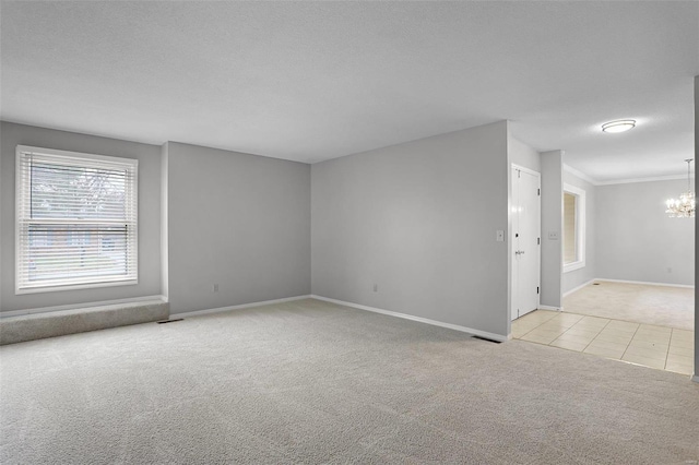 carpeted spare room featuring a textured ceiling, crown molding, and a chandelier