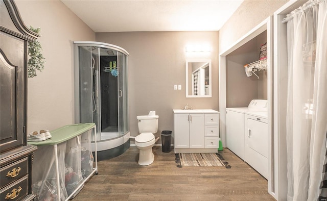 bathroom featuring vanity, washing machine and clothes dryer, hardwood / wood-style flooring, walk in shower, and toilet