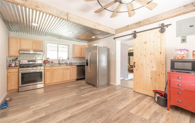 kitchen with a barn door, appliances with stainless steel finishes, light wood-type flooring, and beam ceiling