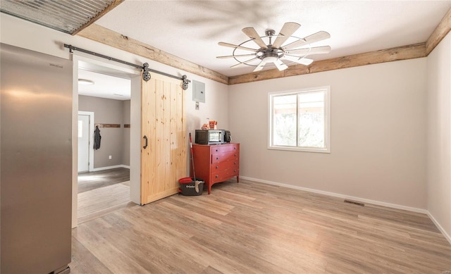 spare room featuring ceiling fan, light wood-type flooring, and a barn door