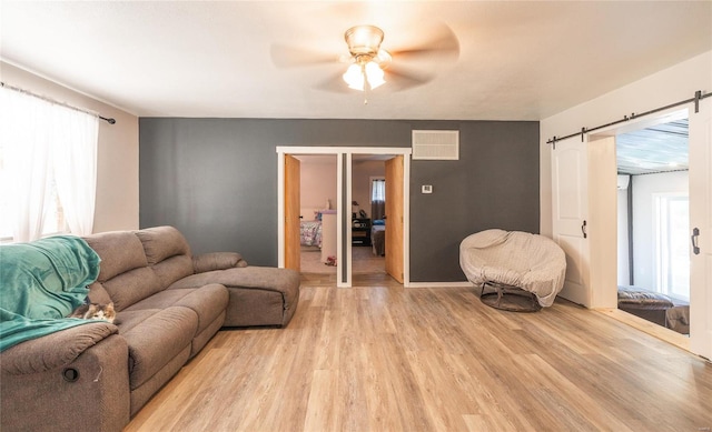 living room with a barn door, ceiling fan, light hardwood / wood-style floors, and a healthy amount of sunlight