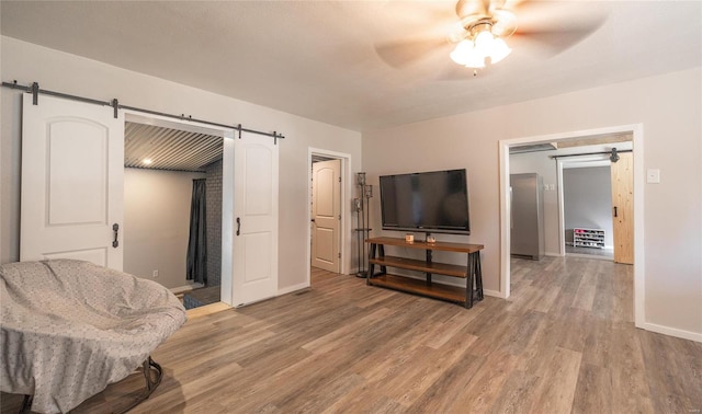 sitting room featuring ceiling fan, a barn door, and wood-type flooring