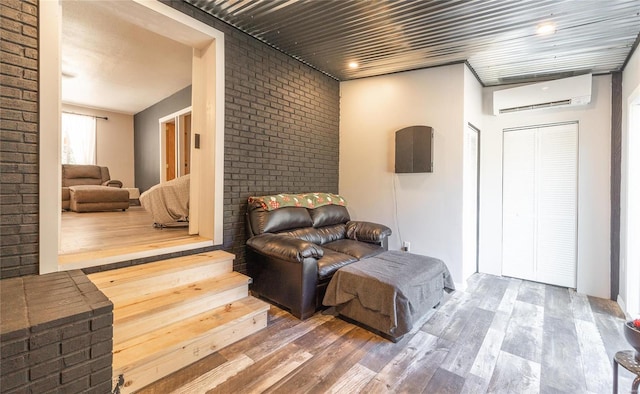 living area featuring hardwood / wood-style flooring, a wall mounted AC, and brick wall