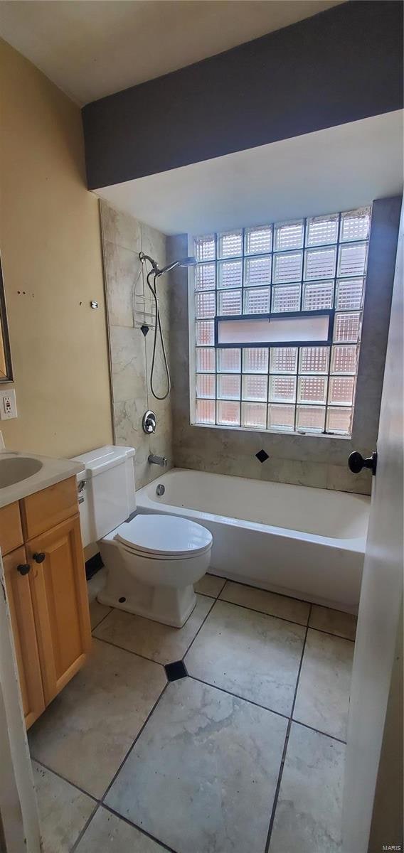 full bathroom with tiled shower / bath, vanity, plenty of natural light, and toilet