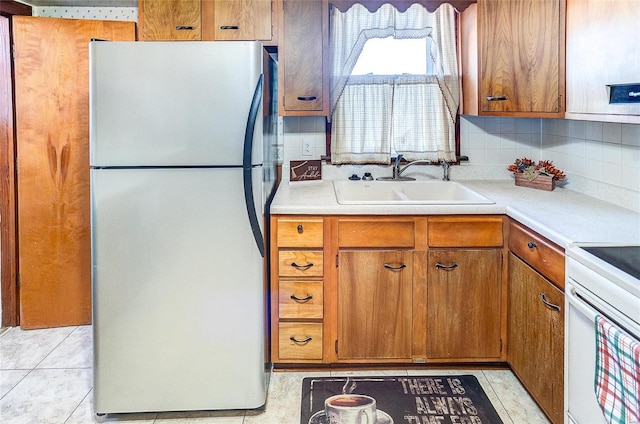 kitchen featuring stainless steel fridge, backsplash, white range with electric stovetop, sink, and light tile patterned flooring