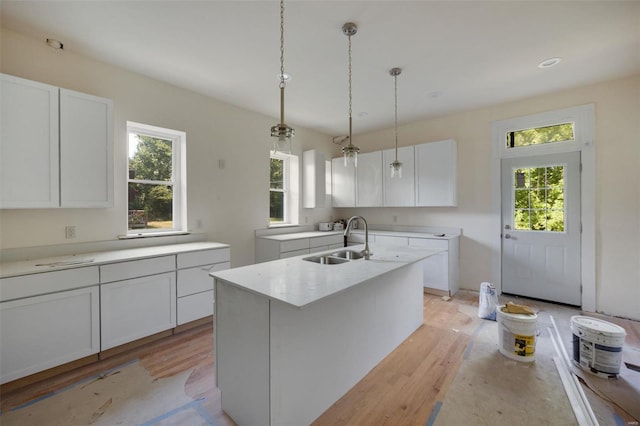 kitchen with light wood-type flooring, white cabinetry, and a kitchen island with sink