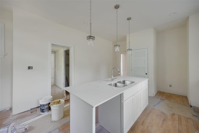 kitchen featuring pendant lighting, white cabinets, sink, a kitchen island with sink, and light hardwood / wood-style flooring