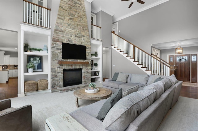 carpeted living room featuring built in shelves, ceiling fan, crown molding, and a fireplace