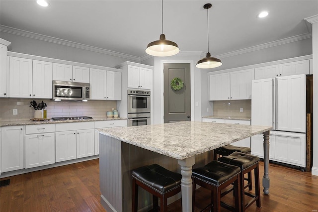 kitchen with pendant lighting, white cabinets, decorative backsplash, appliances with stainless steel finishes, and a kitchen island