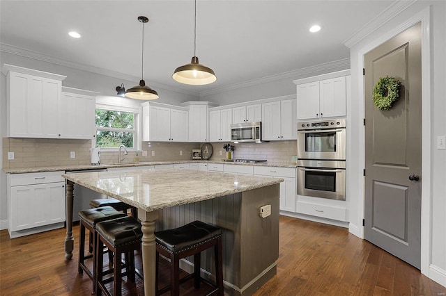 kitchen featuring white cabinetry, sink, a center island, hanging light fixtures, and appliances with stainless steel finishes