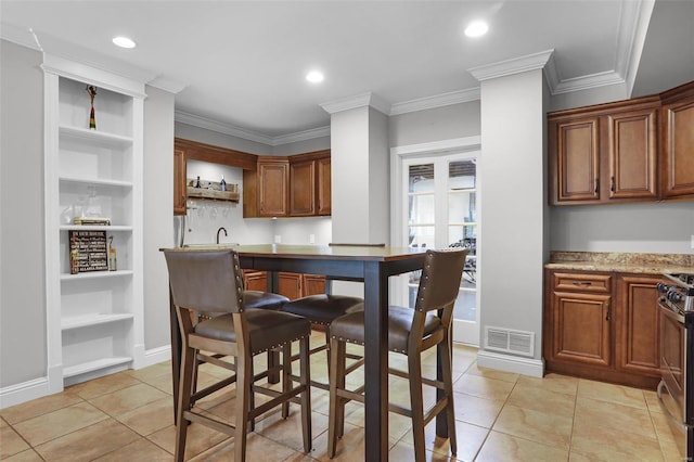 kitchen with stainless steel gas range oven, built in shelves, light stone countertops, ornamental molding, and light tile patterned floors