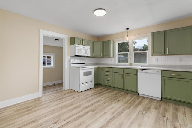 kitchen with decorative backsplash, green cabinets, sink, light wood-type flooring, and white appliances