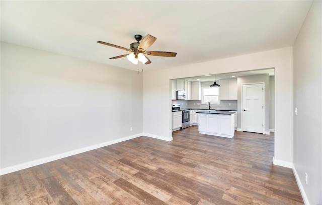 kitchen with dark countertops, appliances with stainless steel finishes, open floor plan, a sink, and baseboards