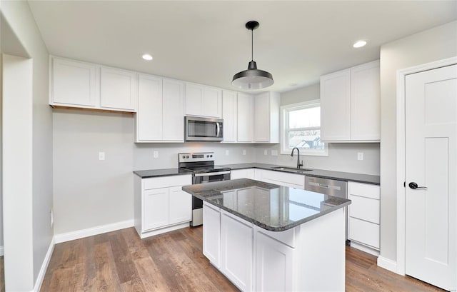 kitchen featuring appliances with stainless steel finishes, white cabinets, a sink, a kitchen island, and baseboards